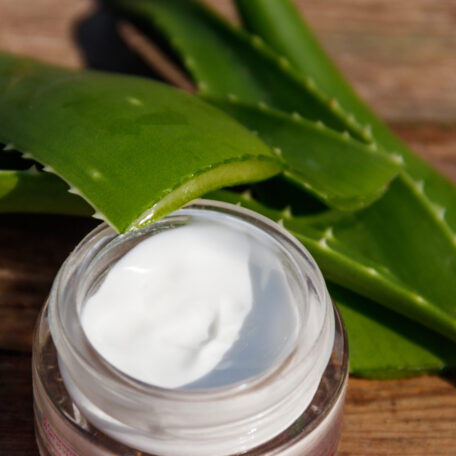 Green leaves of aloe vera plant and moisturizing cream on rustic wooden background